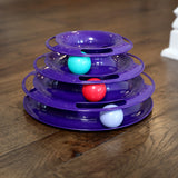 The Quirky Kitty Three Layer Ball Track Cat Toy by Quirky Kitty is a purple, tiered plaything with three levels featuring vibrant turquoise, red, and white balls. It offers engaging interactive play while resting on a polished wooden floor.