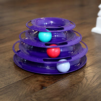 The Quirky Kitty Three Layer Ball Track Cat Toy by Quirky Kitty is a purple, tiered plaything with three levels featuring vibrant turquoise, red, and white balls. It offers engaging interactive play while resting on a polished wooden floor.