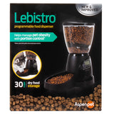 The image shows the Aspen Pet Lebistro Programmable Food Dispenser. With a clear container and digital control base, it holds 30 cups of kibble for portion management to help prevent obesity. A dog eats from it contentedly.