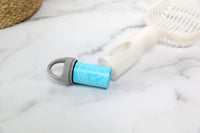 A blue, cylindrical container with a gray handle sits on marble next to a white Arm & Hammer Deluxe 2-In-1 Litter Scoop with Waste Bags, featuring white text and graphics suggesting added freshness from Arm & Hammer baking soda.