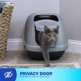 A gray cat exits a Petmate Basic Hooded Cat Litter Pan with a swinging door on a carpeted floor. A wicker basket is on the left. A blue banner at the bottom reads, PRIVACY DOOR FOR BOTH YOU & YOUR CAT, emphasizing easy cleaning and an odor-absorbing filter.