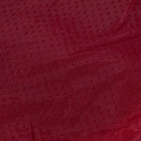 Close-up of the Aspen Pet Self-Warming Oval Lounger Pet Bed featuring a red fabric with a textured dot pattern, resembling faux lambs wool plush. The slightly wrinkled material has a subtle sheen that reflects light, creating a rich, luxurious look.