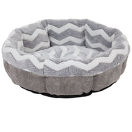 The SnooZZy Round Shearling Bolster Dog Bed by Snoozzy, in gray and white, features a zigzag pattern, plush fabric, and raised sides for comfort. Designed for aging pets, it has a non-skid bottom to ensure stability and safety.