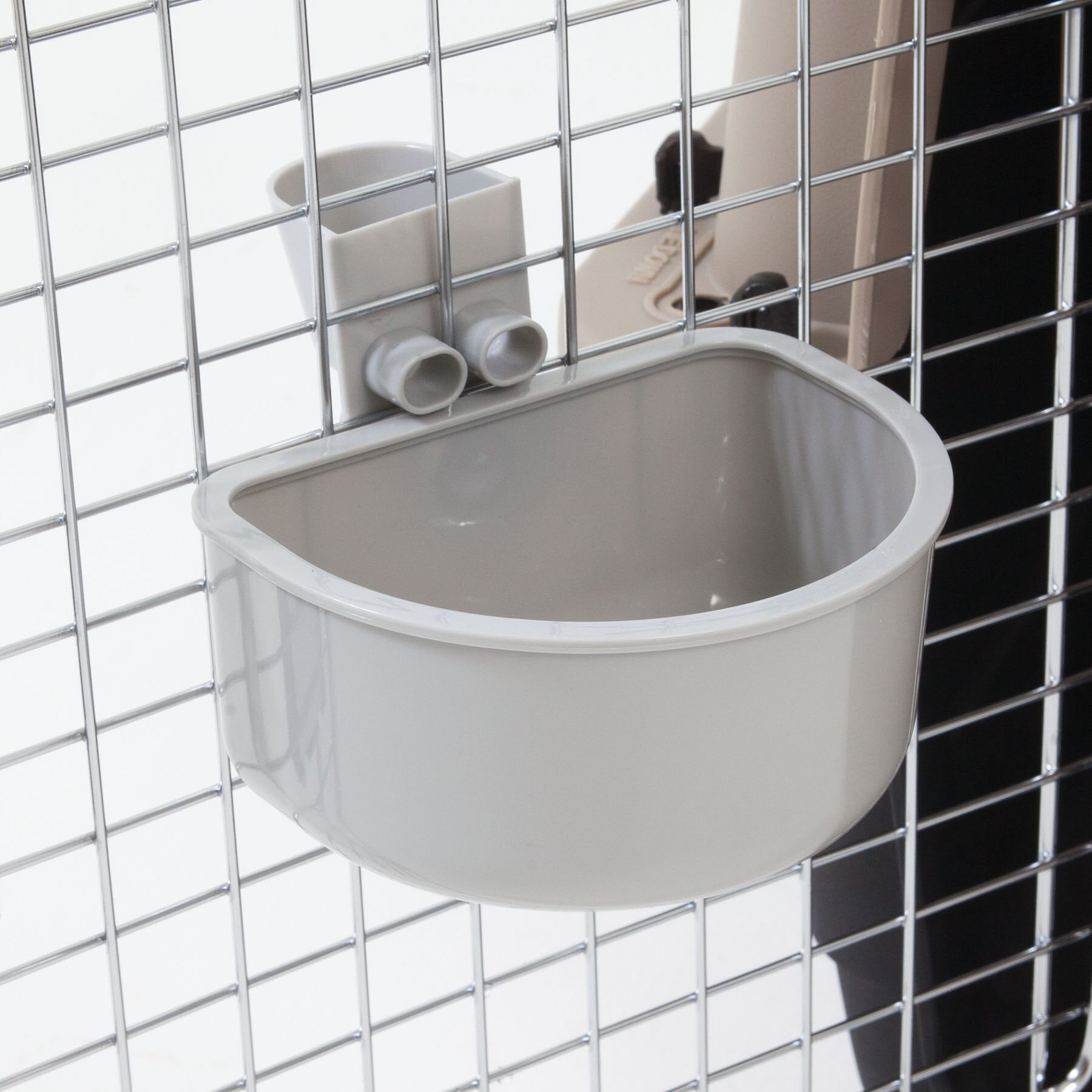 The Petmate No Spill Kennel Cup, in beige, mounts securely to a metal wire cage with square openings using a sturdy bracket. This rounded rectangular bowl from Petmate is perfect for pets and provides convenience as an efficient travel water bowl.