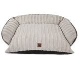The Snoozzy Rustic Luxury Comfy Couch Pet Bed is plush and cream-colored, featuring ribbed fabric and raised sides. A small brown tag with a paw print decorates the front. Its machine washable for easy care, shown empty against a plain white background.