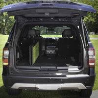 The image shows the open trunk of an SUV parked on grass, featuring a Gen7Pets Natural Step Ramp by Gen7, with both rear seats folded down to maximize cargo space. Trees and a soccer goal are visible in the background.
