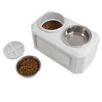 The Vittles Vault Elevated Storage Dog Feeder is shown in white, with two compartments and Gamma Seal Technology for fresh food storage. One compartment holds kibble, while the other is empty. A lid rests nearby, and an extra bowl filled with kibble sits beside the feeder.