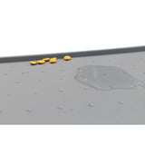 A gray PetFusion Pet Food Mat made from FDA-grade premium silicone with anti-slip bumps displays scattered yellow pills on the left and a puddle of clear liquid on the right.