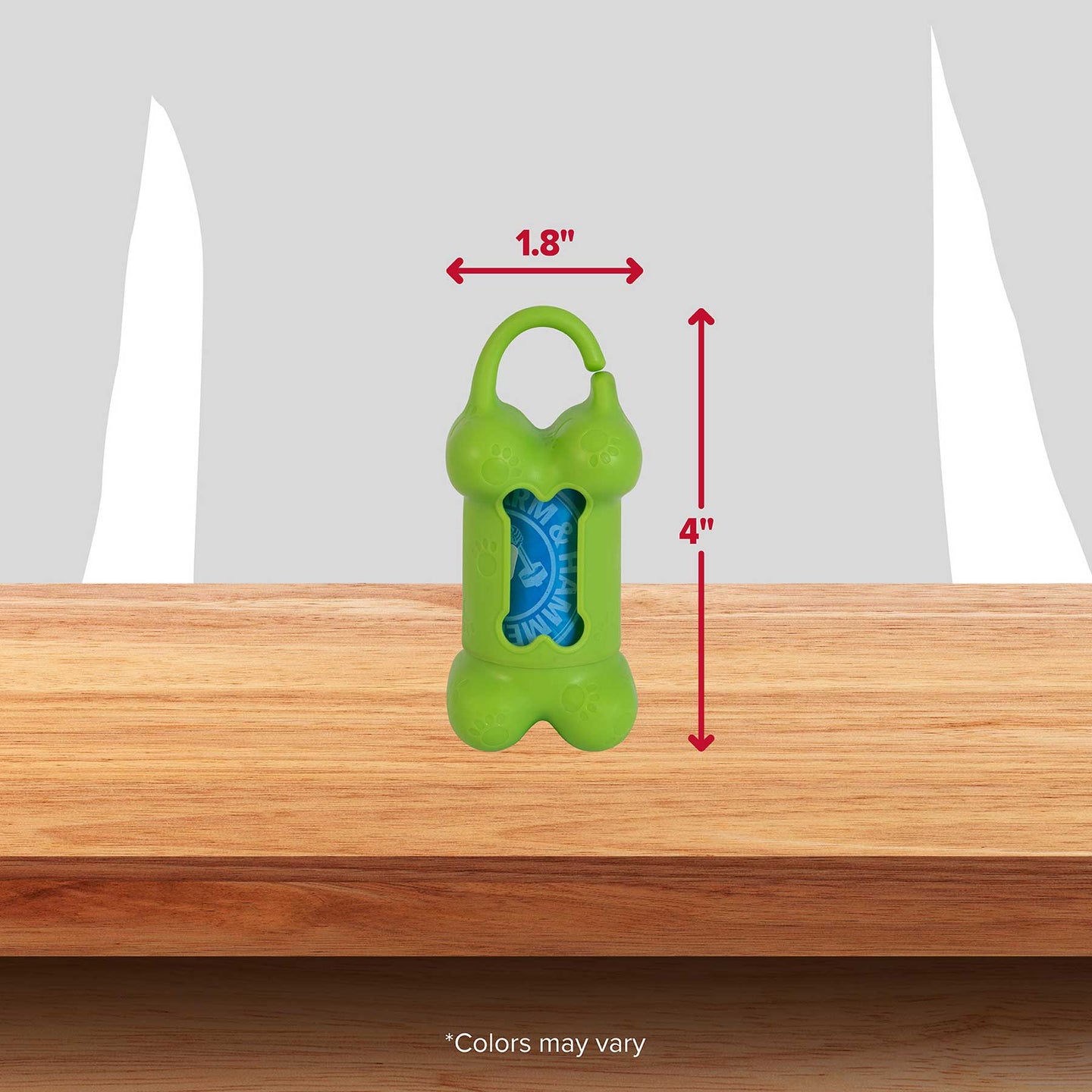 The Arm & Hammer Bone Dispenser & Disposable Waste Bag Set, designed in green and shaped like a bone, measures 1.8 wide by 4 tall with a blue bag roll that controls odors. It features a top clip and is displayed on wood against a gray backdrop. Note: Colors may vary.