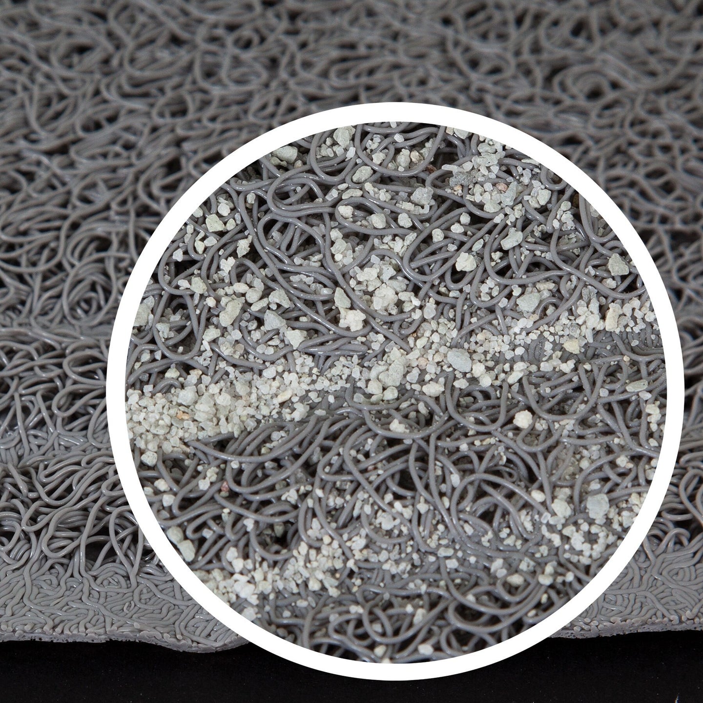 The close-up of the Petmate Litter Mat Circles Design by Petmate shows a textured gray surface with tangled loops resembling spaghetti, featuring a subtle webbed design. A circular area highlights small particles scattered over the loops, creating a speckled look against the solid black background.